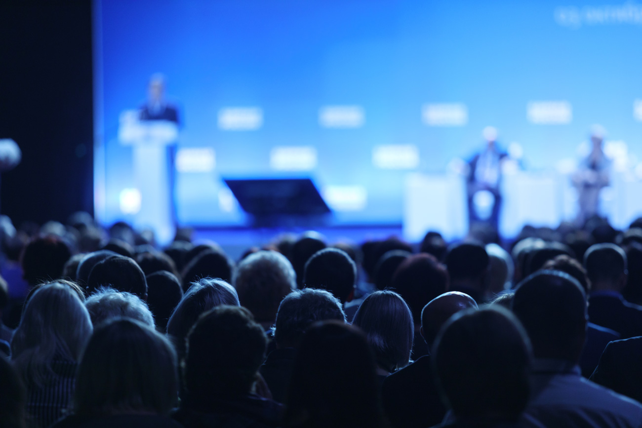 Crowd facing conference stage and speaker at podium